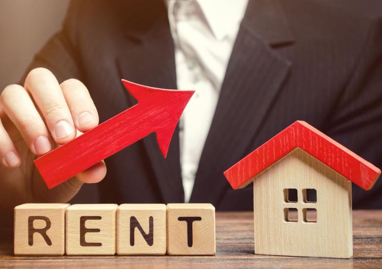 Man holding upward arrow over wooden house and ‘RENT’ blocks, showing rental growth