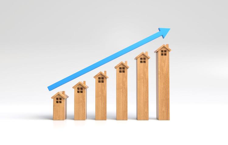 Wooden blocks of houses placed in ascending order with a blue upward arrow above them, indicating market growth.