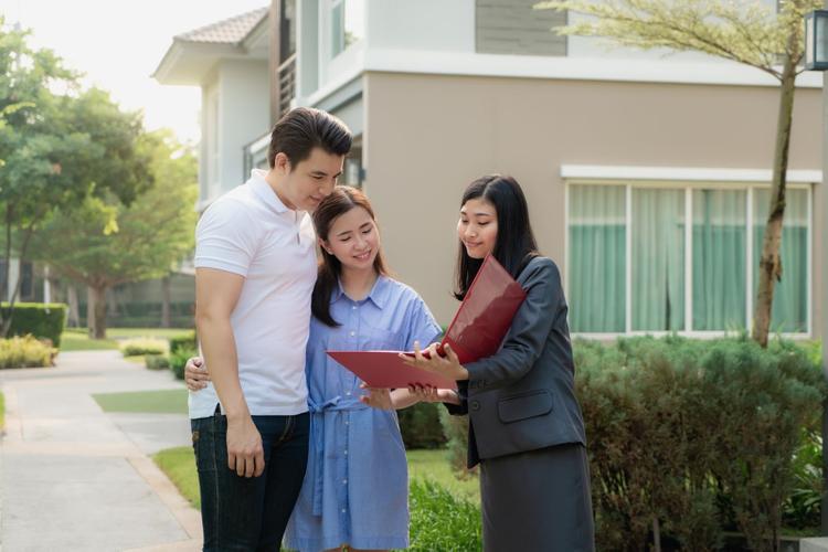 A female real estate agent showing house details in her file to a young couple interested in buying it.