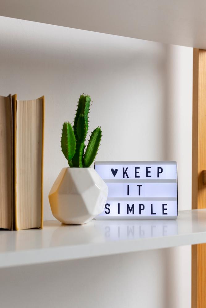 Close-up of a shelf with books, a potted plant, and a decorative piece that says “Keep It Simple”.