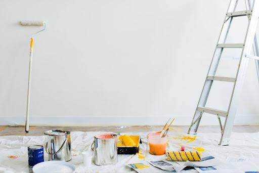 Paint buckets on the floor, a ladder, and a roller prepared for painting a room during home renovation.
